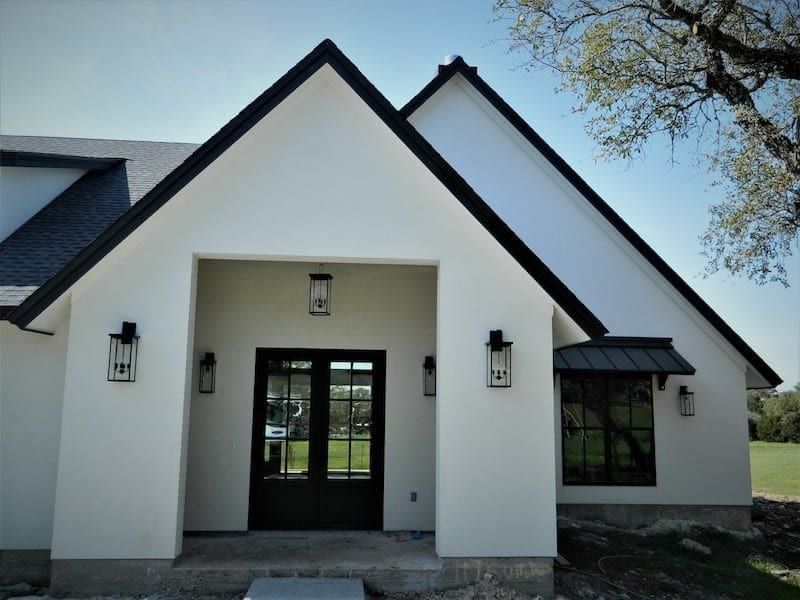 Front entry of the finished house, with white stucco gables, a black double door and lantern sconces