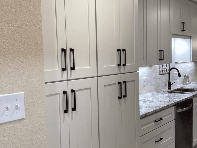 Floor-to-ceiling white pantry cabinets with black pulls, beside the counter and sink