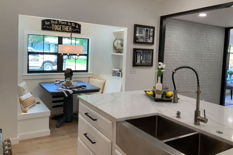 Kitchen island in white marble with a double stainless sink, and a breakfast nook under a black steel casement window