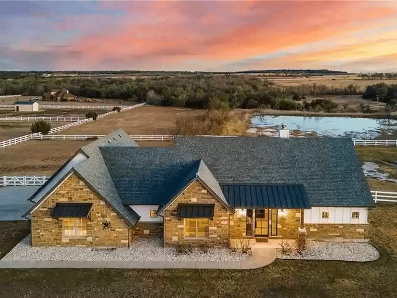 Aerial view at dusk of the house on its acreage, with white rail fencing and a pond behind it