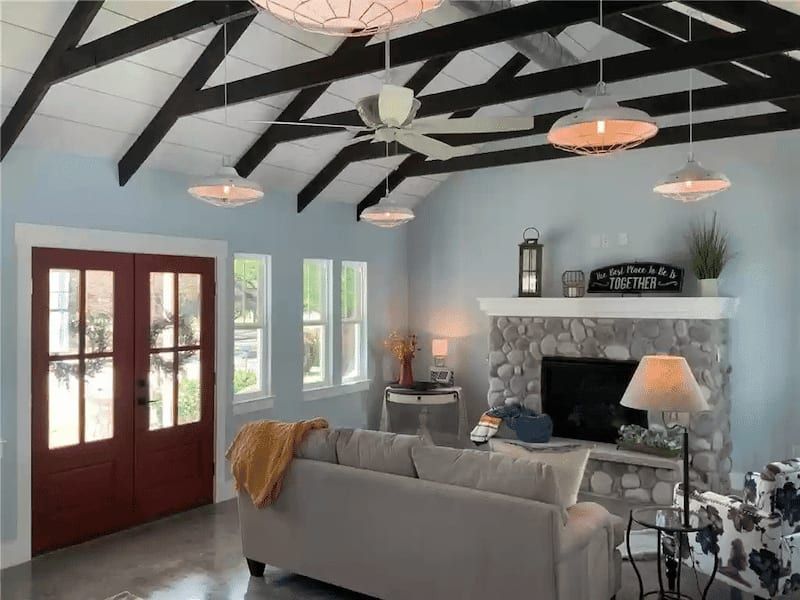 Living room under a vaulted ceiling with dark exposed beams, a river rock fireplace and red double front doors