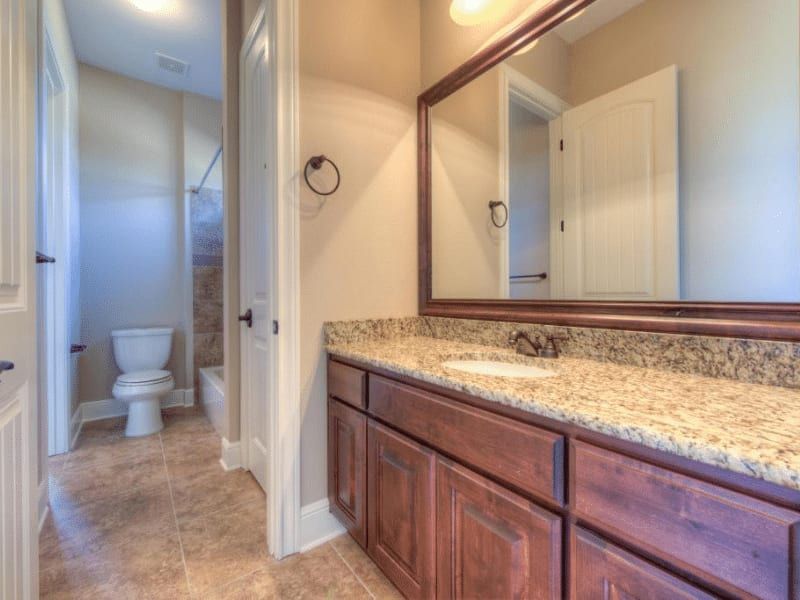 Bathroom with a stained wood vanity, a granite top, a framed mirror and a tub beyond the doorway