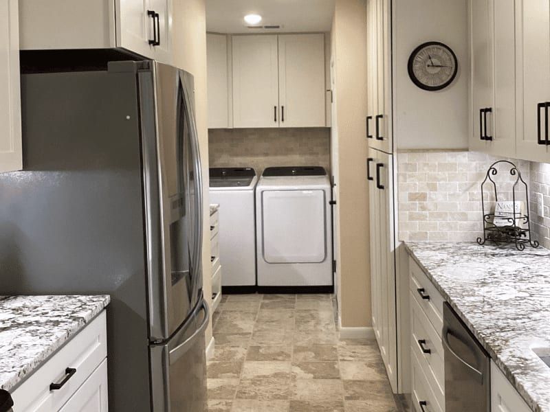 Laundry room brought in from the garage, with a washer and dryer under white cabinets at the end of the kitchen