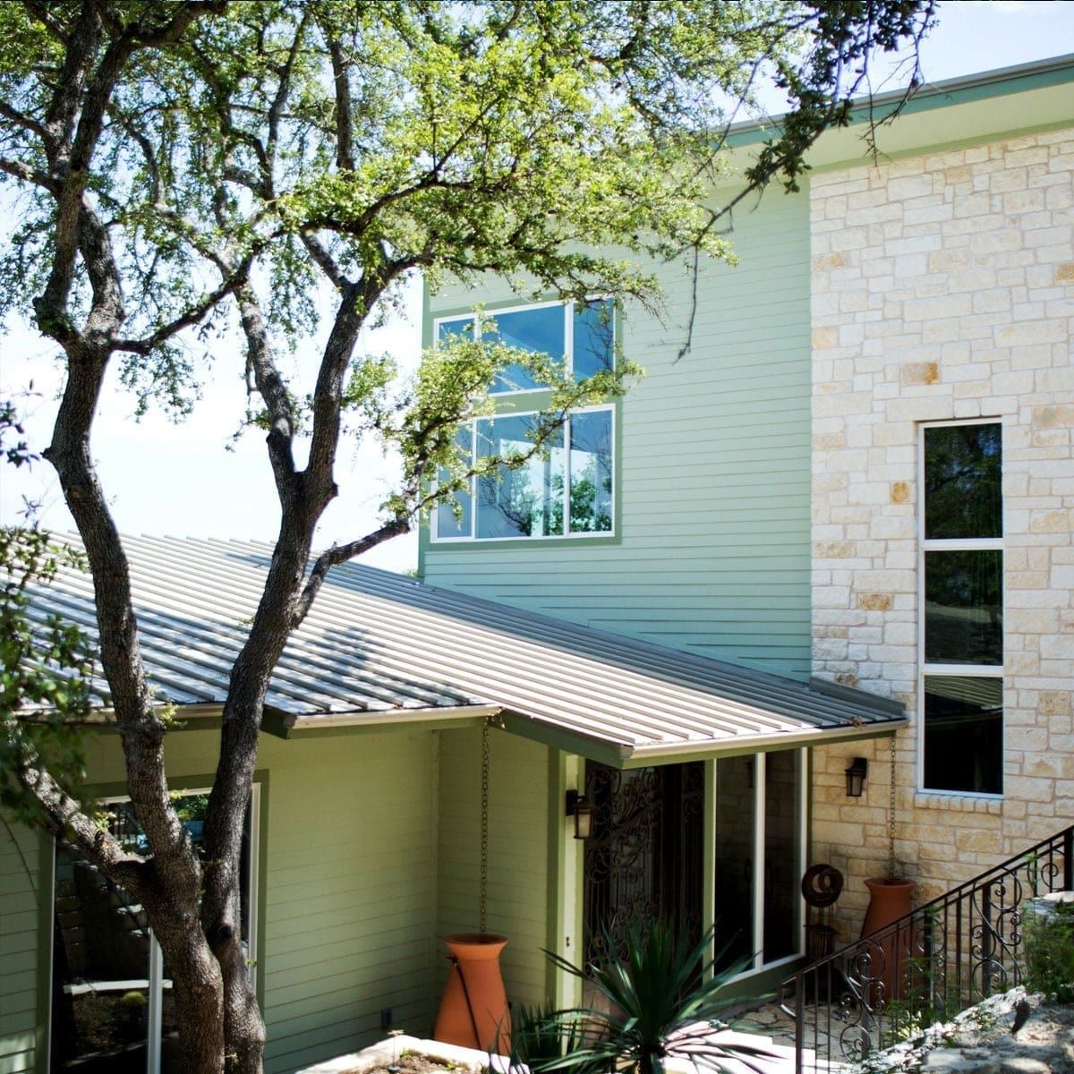 Three-story elevation in green siding and Texas limestone, with a standing seam roof and a rain chain