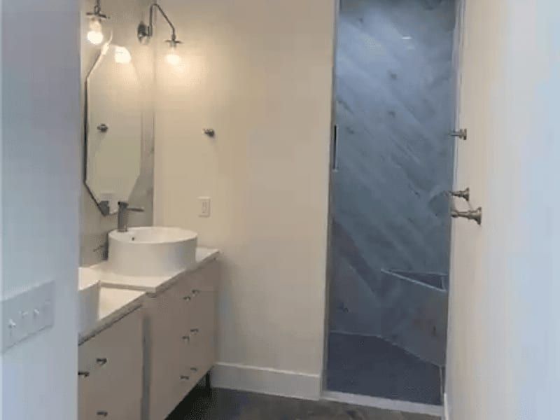 Bathroom with a vessel sink, wall-mounted lights and a walk-in shower tiled in grey marble with a built-in bench