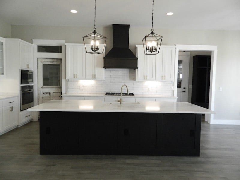 Kitchen with white cabinets, a black island, a black range hood and lantern pendants over white marble