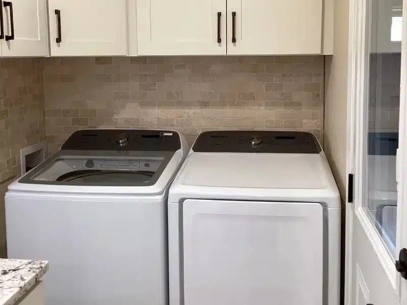 Laundry room with washer and dryer under cabinets and tile backsplash in Austin, TX home