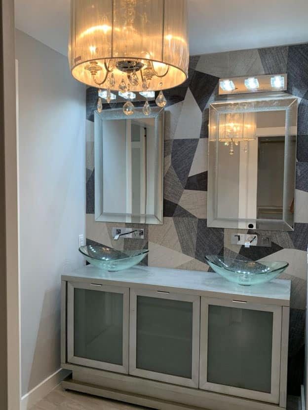 Double vanity with glass vessel bowls, mirrored frames and a grey geometric feature wall