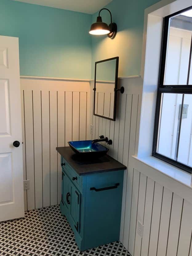 Bathroom with a teal vanity, a blue vessel sink, white beadboard wainscot and patterned black and white floor tile