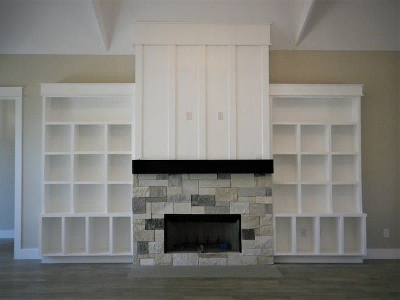 Living room fireplace in stacked stone with a dark timber mantel, flanked by white built-in shelving