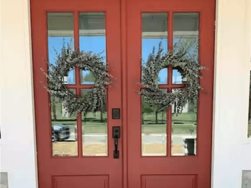 Red double front doors with divided glass panes and matching dried wreaths, seen from the covered porch