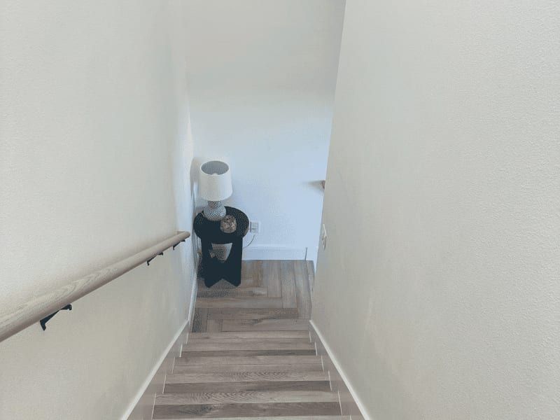 Stairway down from the game room, with a wood handrail and herringbone flooring at the landing