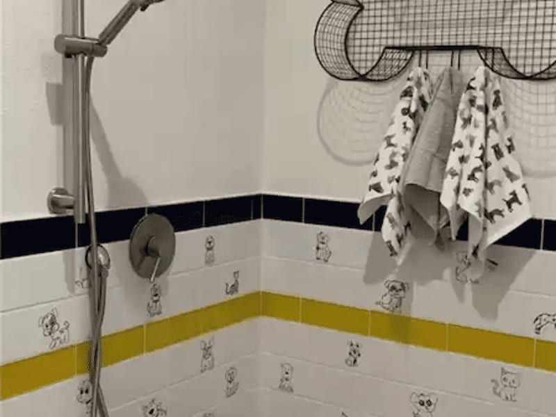 Children's bathroom shower tiled in navy and yellow bands with a border of cat and dog tiles