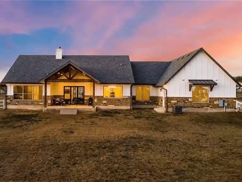 Rear elevation at dusk, with a covered porch under exposed timber and the windows lit