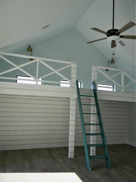Loft above the living room, with a turquoise ladder, a white X-rail balustrade and shiplap walls