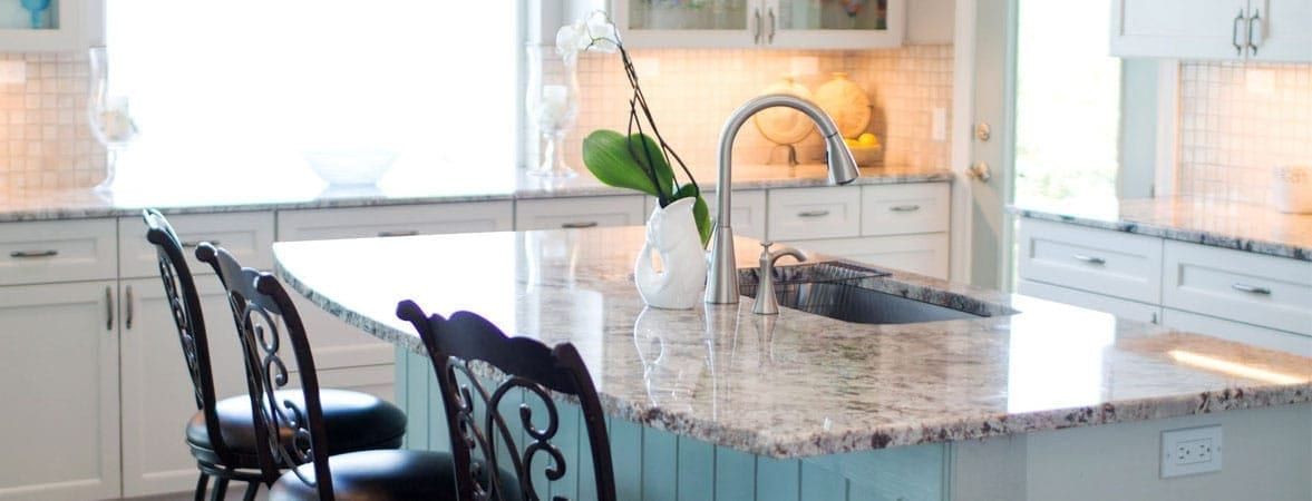 Kitchen island in granite with a pale blue beadboard base and dark scrollwork stools