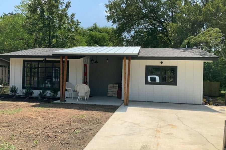 Front of the remodeled house in Taylor, TX, with white board-and-batten siding, a standing seam porch roof and cedar posts