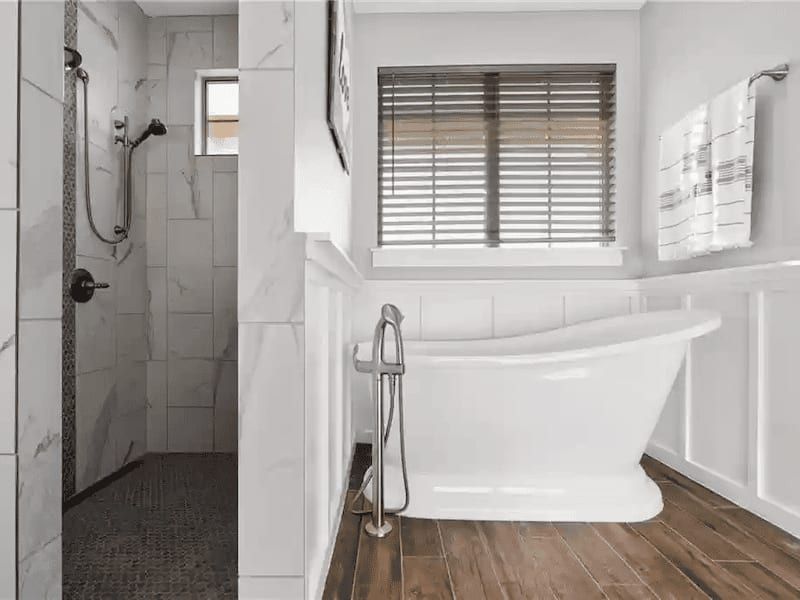 Primary bathroom with a freestanding slipper tub, board-and-batten wainscot and a walk-in marble-tiled shower