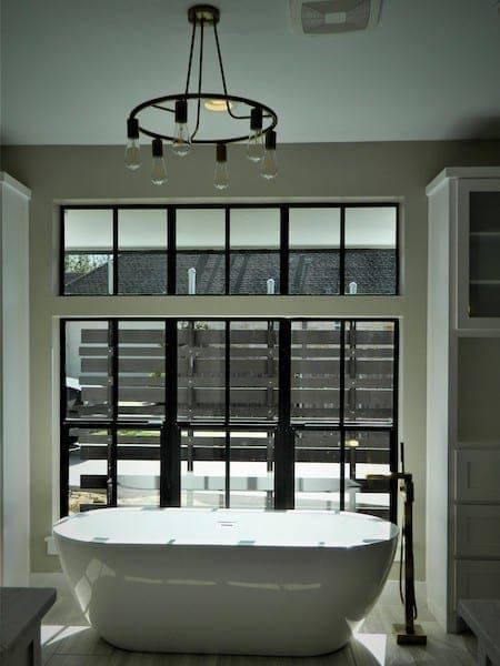 Freestanding tub before large windows with modern chandelier in Austin, TX bathroom
