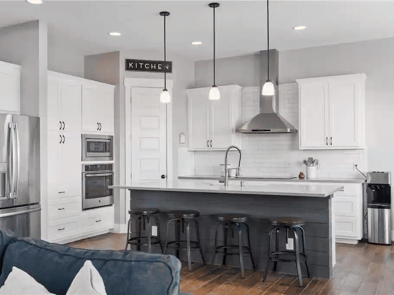 Kitchen with white cabinets, a grey shiplap island seating four and a stainless range hood
