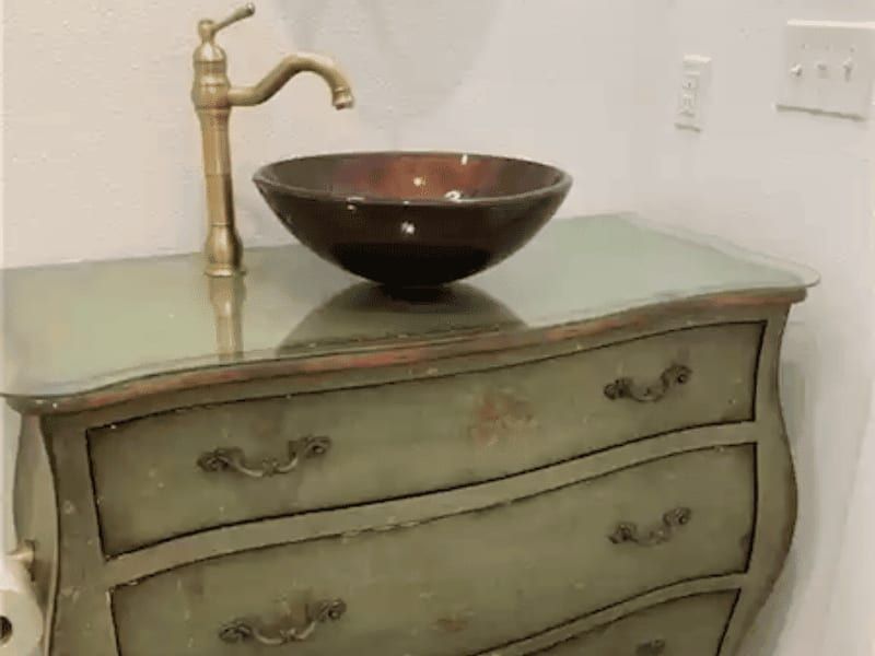 Powder room vanity built from an antique green dresser, with a bronze vessel bowl and a brass faucet