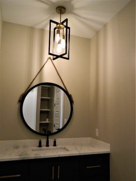 Powder room with a dark vanity, a marble top and a round mirror hung from a rope below a lantern pendant