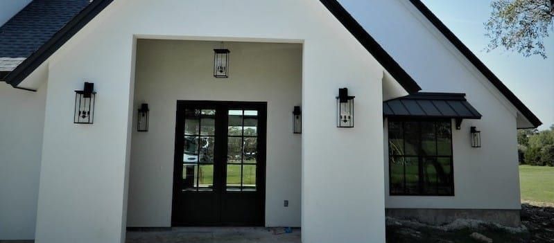 Front entry under white stucco gables, with a black double door flanked by lantern sconces