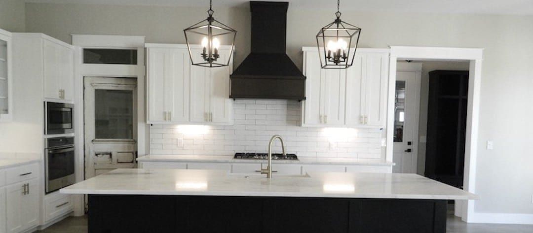 Kitchen with white cabinets, a black island in white marble and lantern pendants overhead