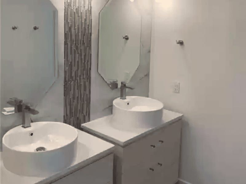 Double vanity with two white vessel bowls, hexagonal mirrors and a vertical glass tile strip between them