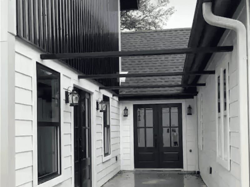 Covered breezeway between two wings of the house, with white lap siding, dark trim and lantern sconces