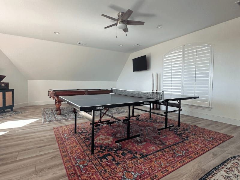 Game room above the garage with a ping-pong table, a pool table and a shuttered arched window