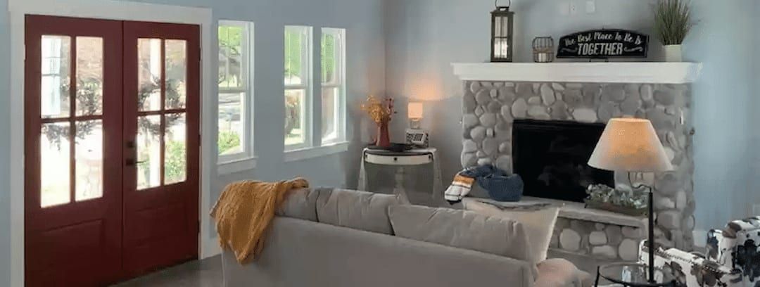 Cozy living room featuring a stone fireplace, gray couch, and red double doors at Austin, TX