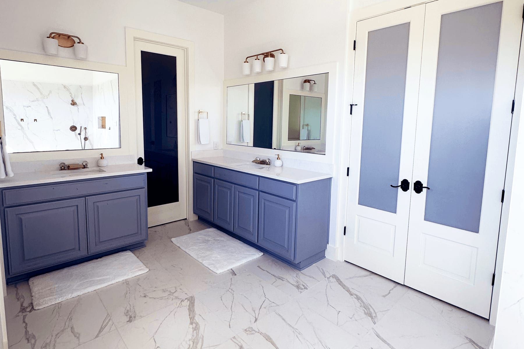 Double vanity in a Leander primary bath with blue cabinetry and marble-look floors