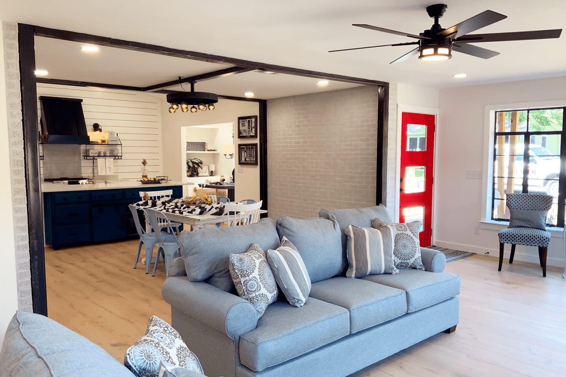 Remodeled living room opening onto the new kitchen, with a painted brick wall and wide-plank floors