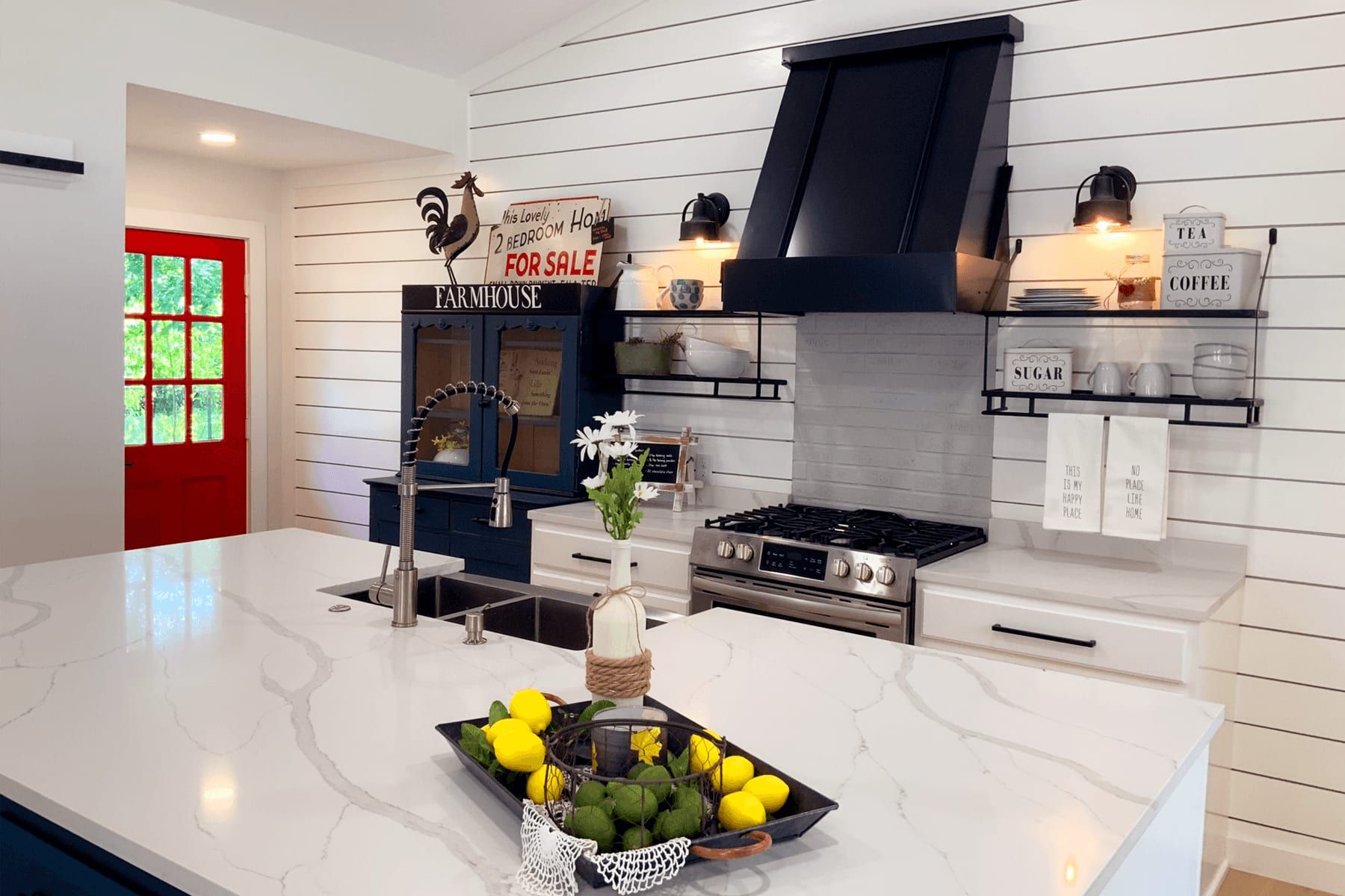 Open kitchen detail: quartz island, shiplap wall, black range hood, and a red front door beyond