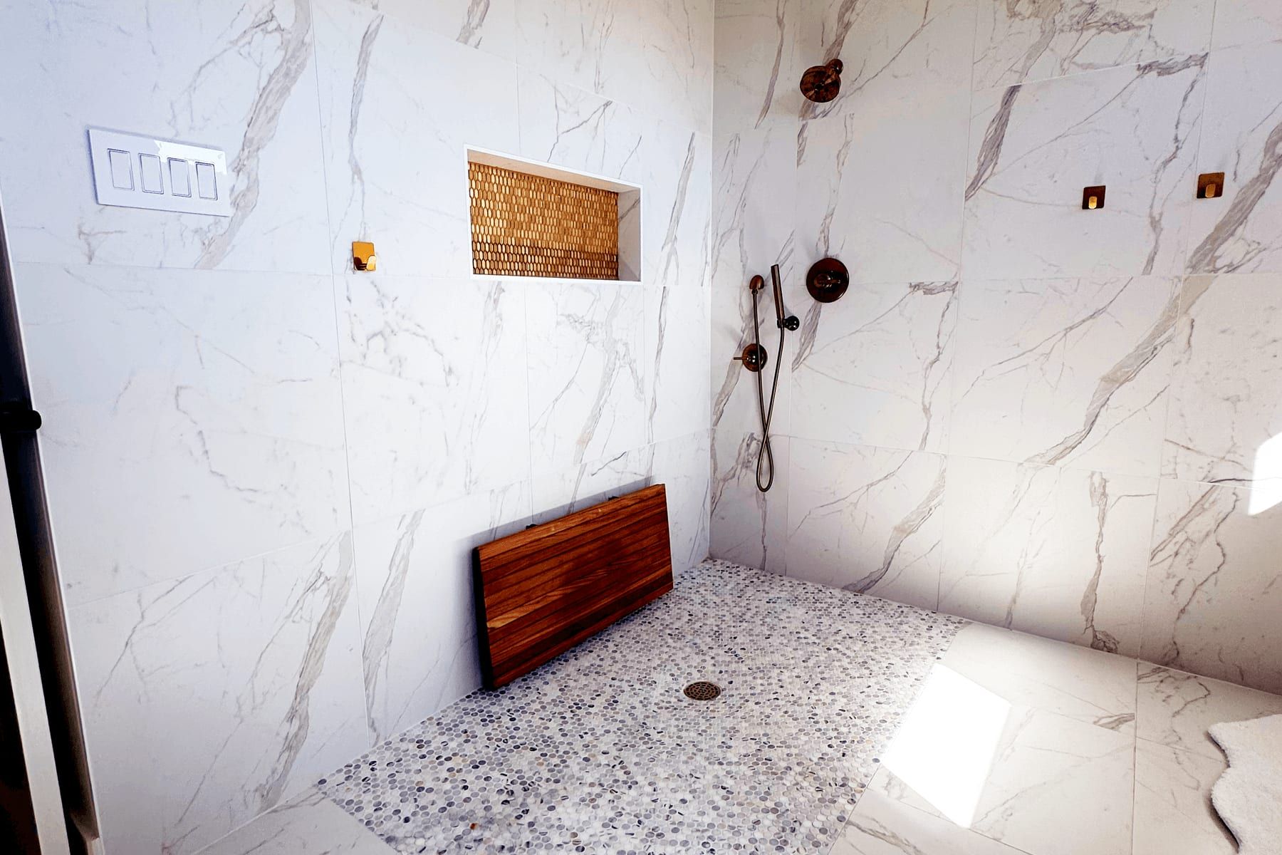 Curbless walk-in shower in Leander with marble-look tile, a niche, and a teak fold-down bench