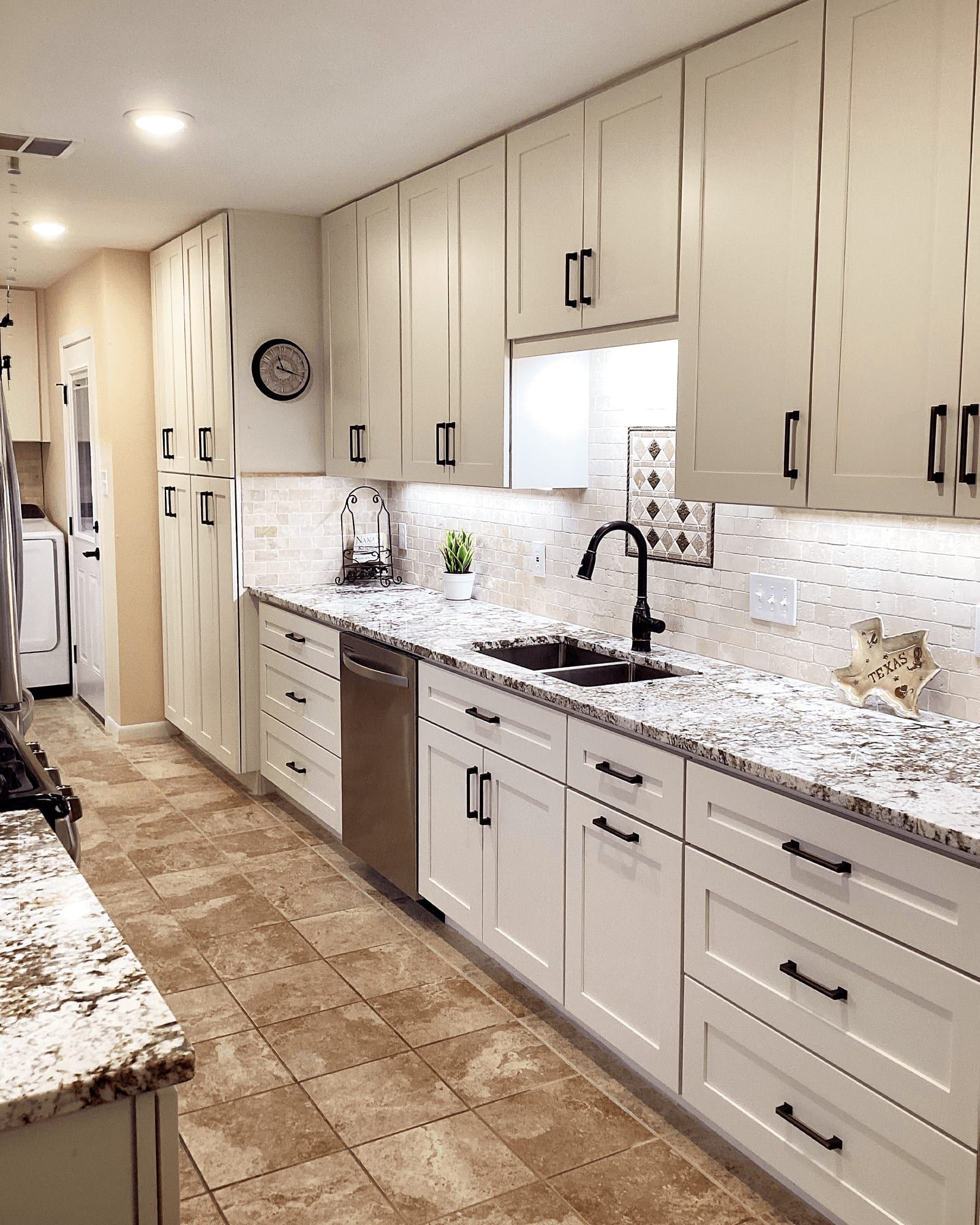 The same kitchen after the remodel, with white shaker cabinetry, granite counters, tile backsplash, and new flooring