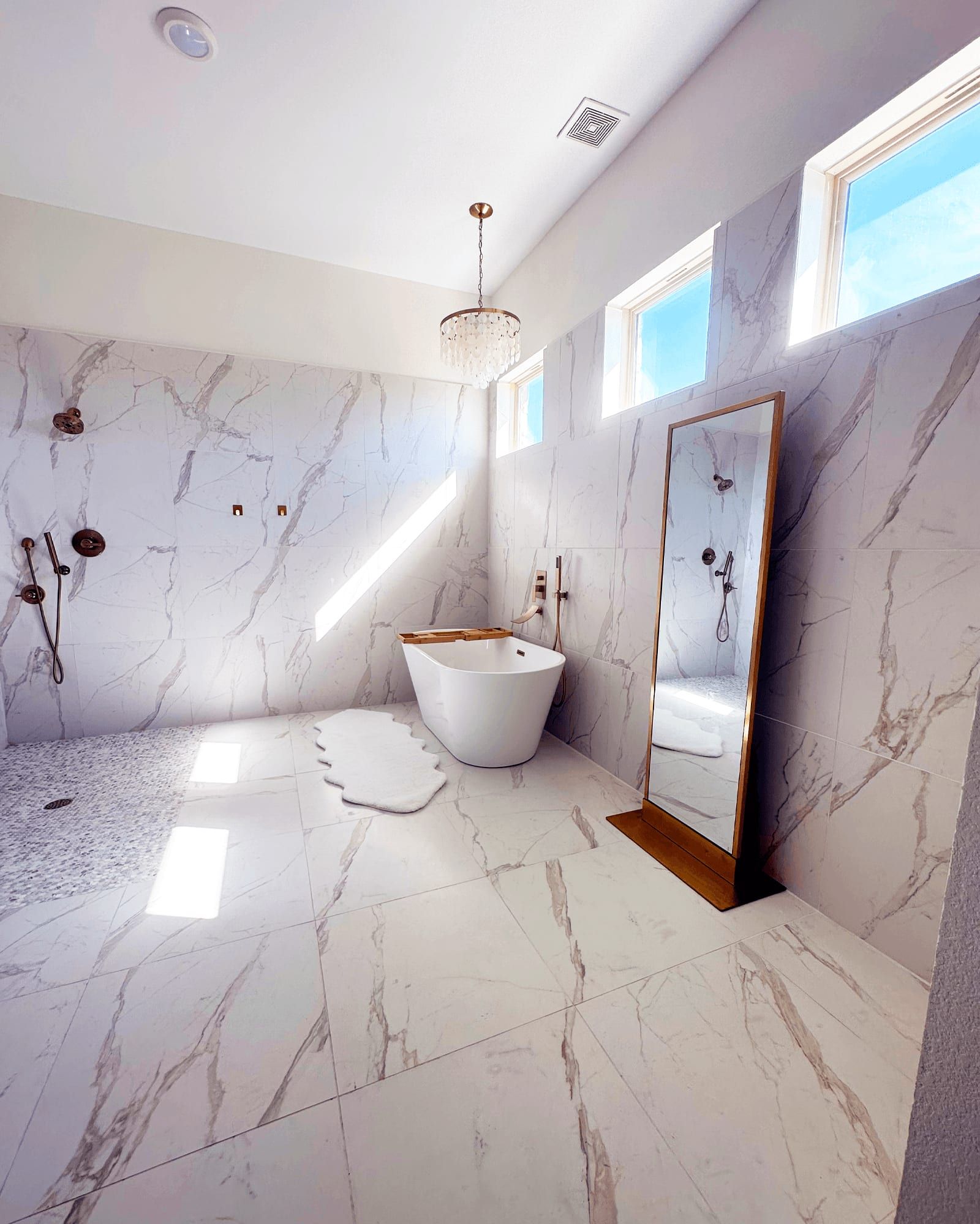 The remodeled primary bath with a freestanding tub, marble-look porcelain tile, and clerestory windows