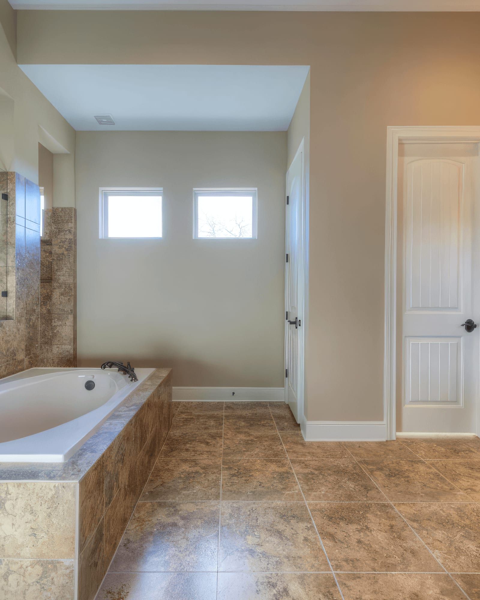 Primary bath before the remodel: beige tile, a built-in tub deck, and a dark wood vanity