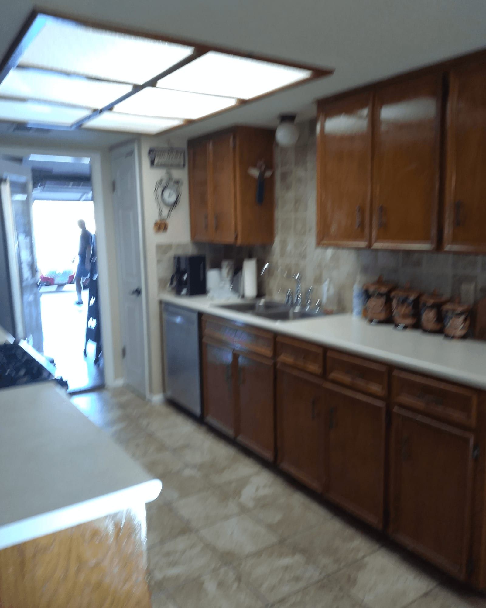 Kitchen before the remodel, with dark wood cabinets, a fluorescent ceiling box, and a narrow galley layout