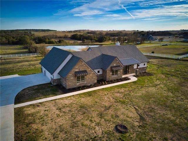 A finished Flenn custom home on acreage, seen from above, with a stock pond beyond it